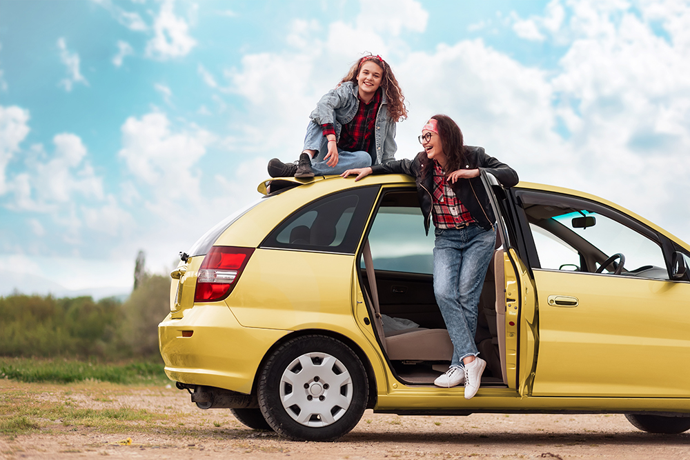 two young women smiling with their yellow hatchback car | Metro East, IL